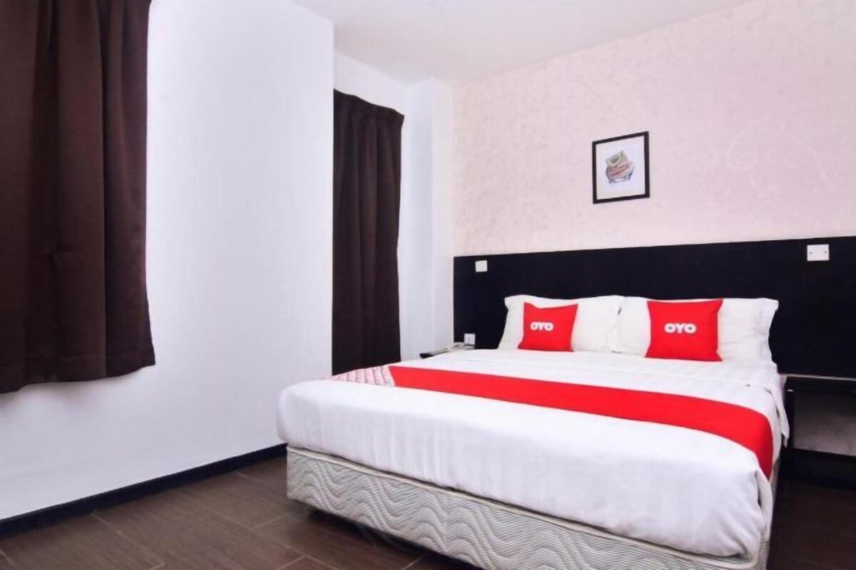 Una habitación de hotel con cama, cabecera, un cuadro enmarcado en la pared y cortina.