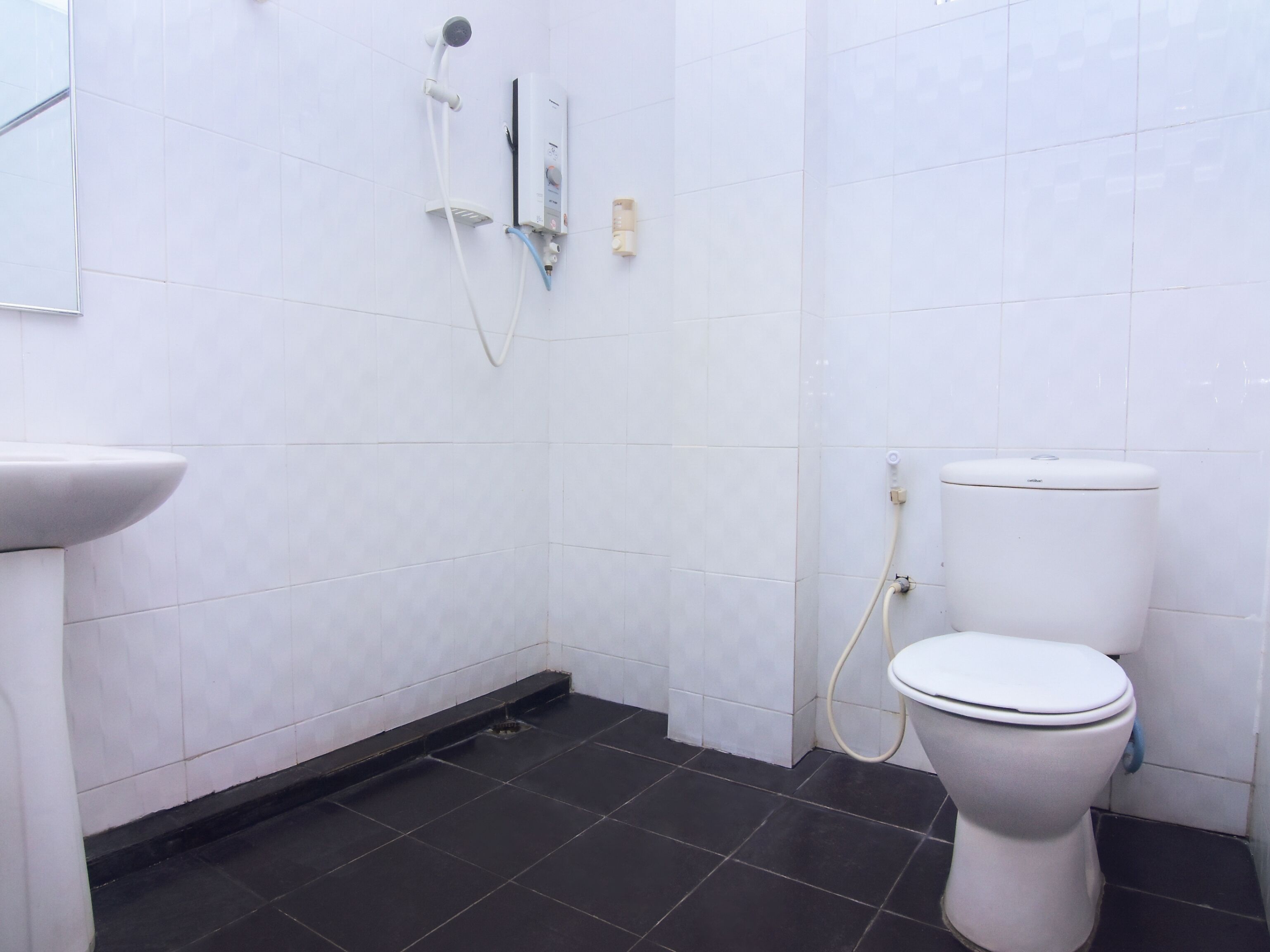 A bathroom with white tiles, a black floor, a white toilet, and a shower unit.