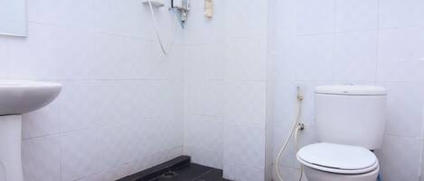 Un baño con azulejos blancos, suelo negro, inodoro blanco y cabina de ducha.