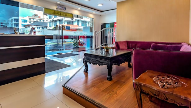A hotel lobby with a reception desk, a red sofa, a wooden coffee table, and a view of the street outside.