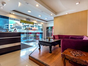 Eine Hotellobby mit einer Rezeption, einem roten Sofa, einem Holztisch und Blick auf die Straße.