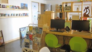 Una habitación con dos escritorios, cada uno con una computadora y teclado, dos sillas verdes y un estante con libros y revistas.
