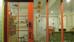 Zona de recepción con un cartel que dice 'Welcome', un mostrador con computadora y una estantería.