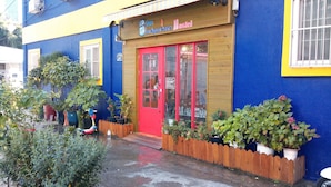 Un hostal Blue Backpackers con una puerta roja, valla de madera y plantas en macetas.
