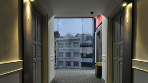 A hallway with patterned carpet, double doors, and a view of buildings in the background. - DREAMTEL Jakarta (Jakarta)