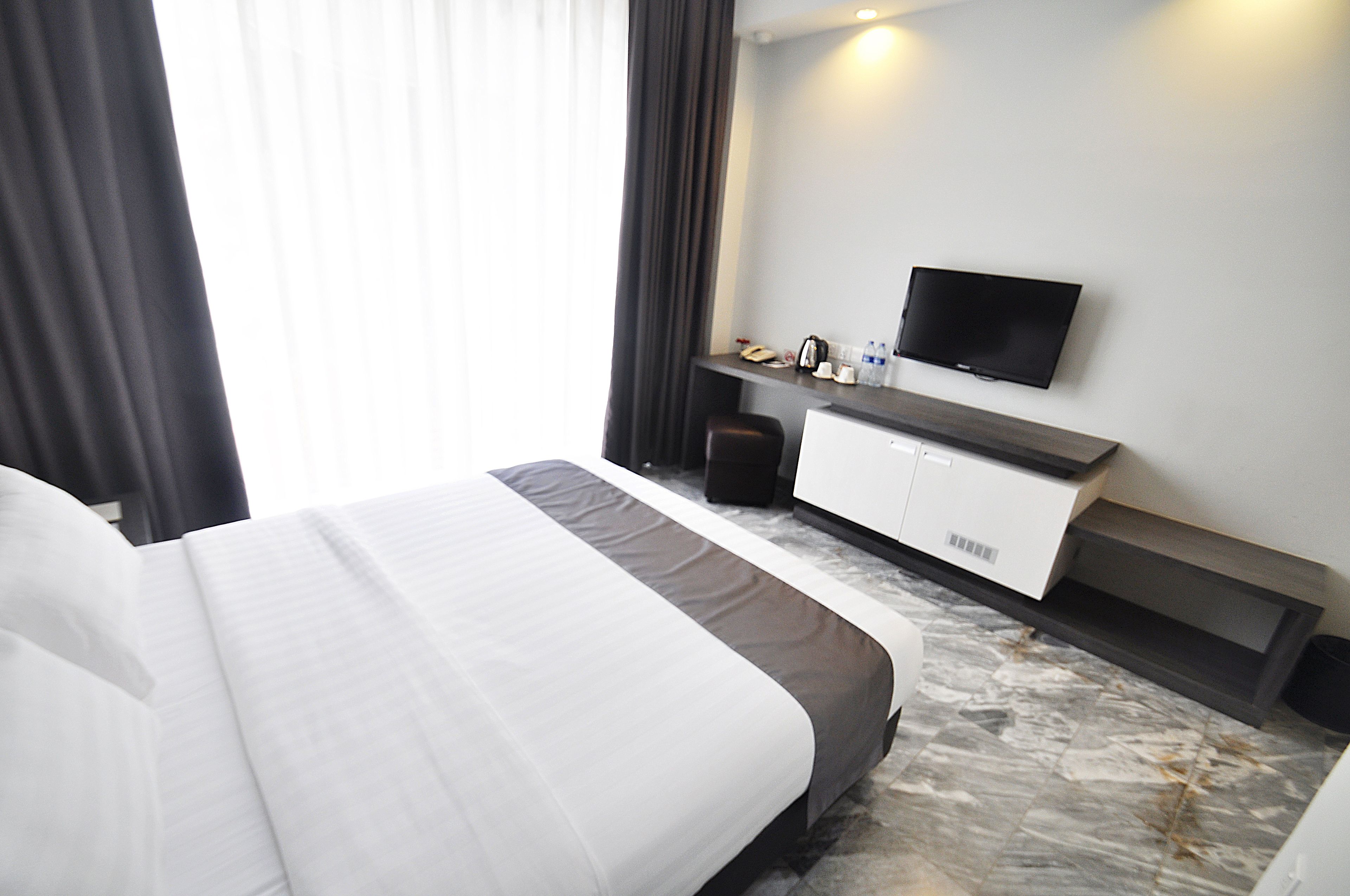 A hotel room with a bed, a desk, a television, and a window with curtains.