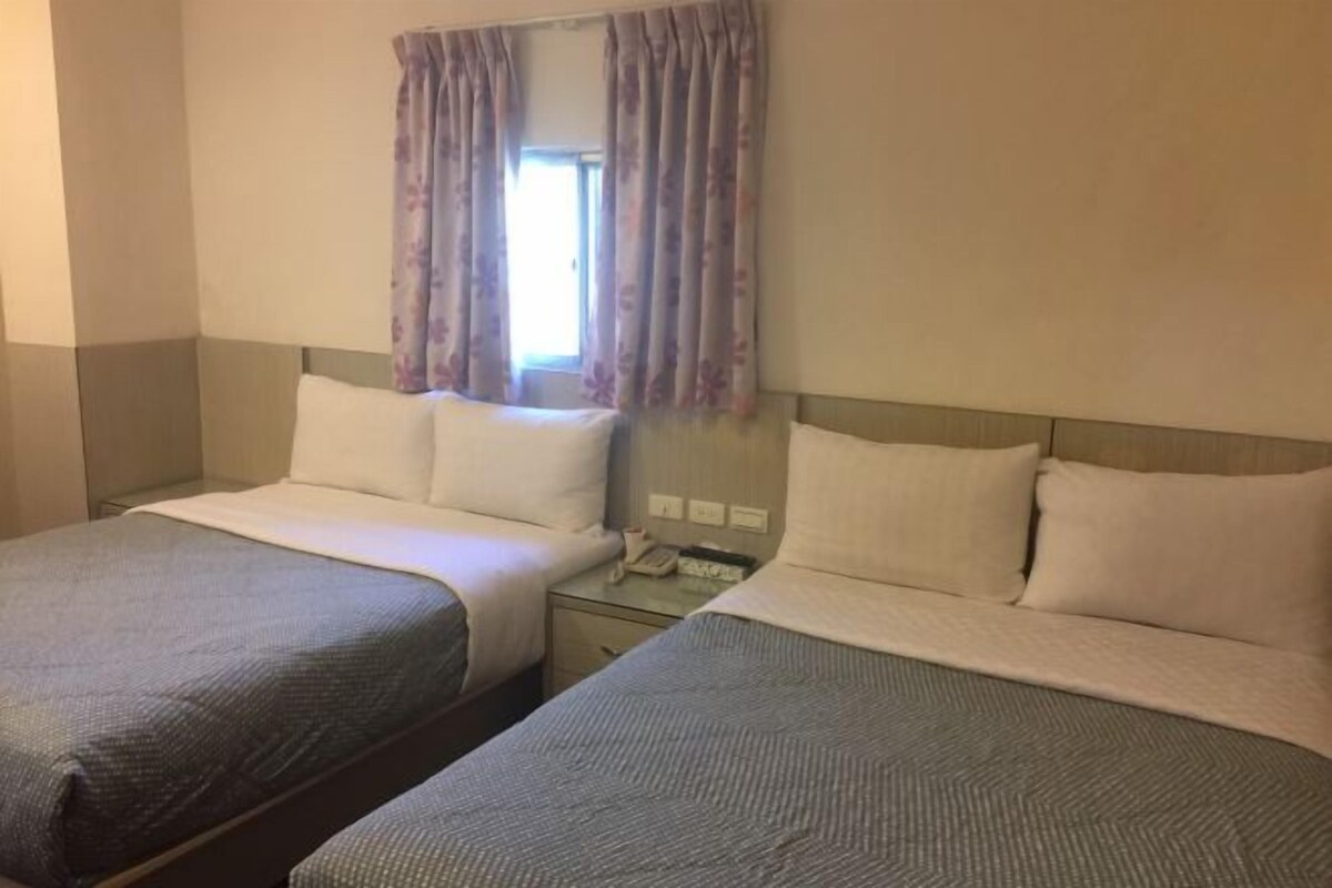 A hotel room with two single beds, a small table, and a window with curtains.