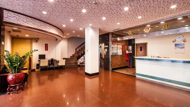 A hotel lobby with a curved reception desk, a staircase, and a potted plant.
