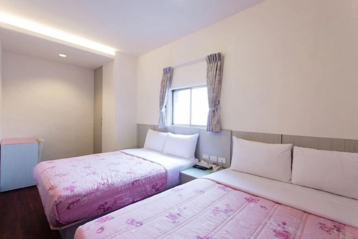 Une chambre d’hôtel avec deux lits, une fenêtre avec des rideaux et une table de chevet.