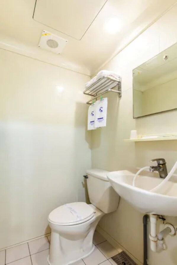 Une petite salle de bain propre, équipée de toilettes, d’un lavabo et d’un miroir. Deux distributeurs de gel hydroalcoolique sont fixés au mur.