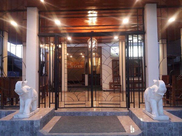 L’entrée d’un hôtel, avec une porte en verre, deux statues de lions blancs et une enseigne sur laquelle on peut lire « OS HAVEN ».