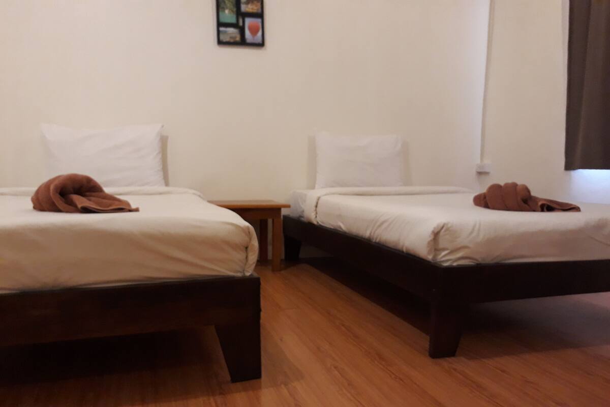 A hotel room with two beds, wooden flooring, and a small table between them.