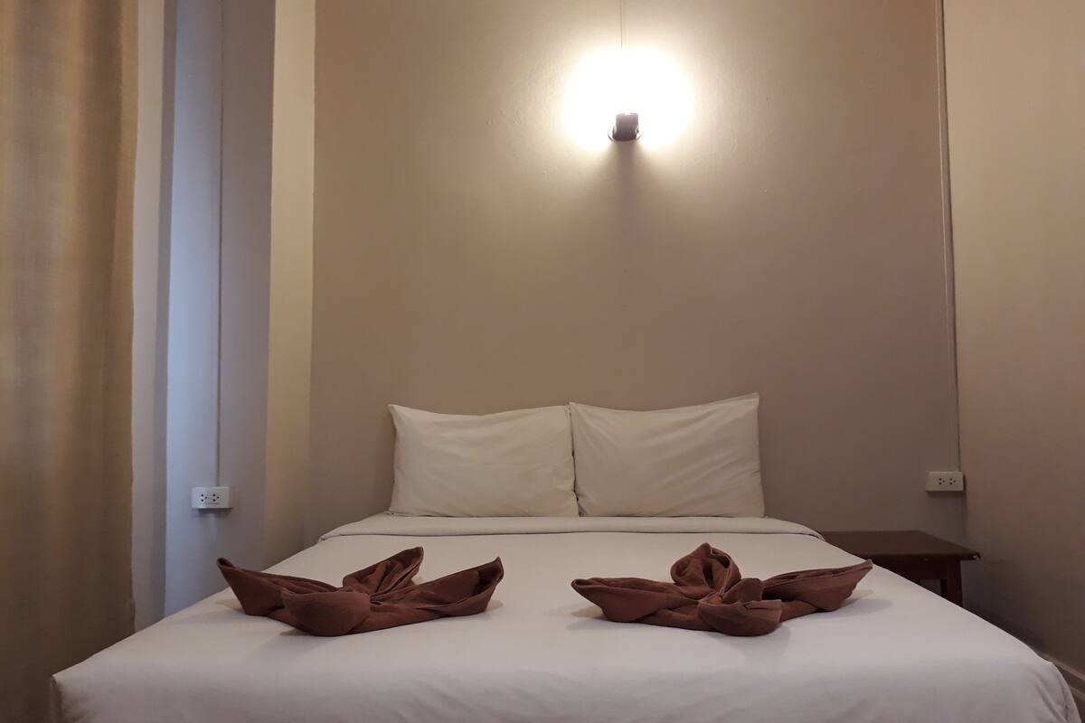 A hotel room with a bed, two pillows, a bedside table, and a wall-mounted light fixture.