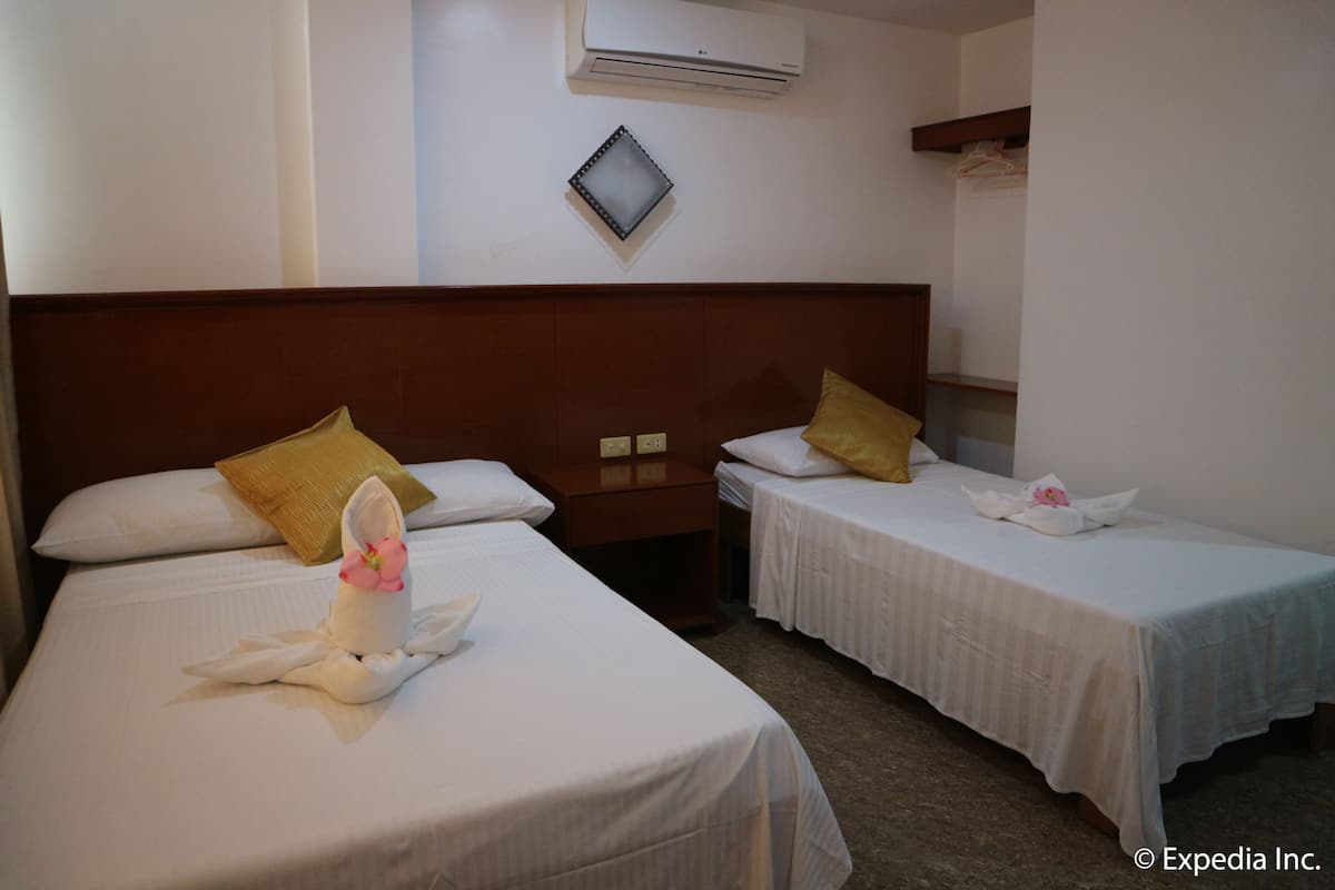 A hotel room with two single beds, a wooden headboard, a wall-mounted air conditioner, and a small shelf with a mirror and a hanging garment.\n\nVerification: The image clearly shows the two beds, wooden headboard, air conditioner, and shelf with a mirror and hanging garment.