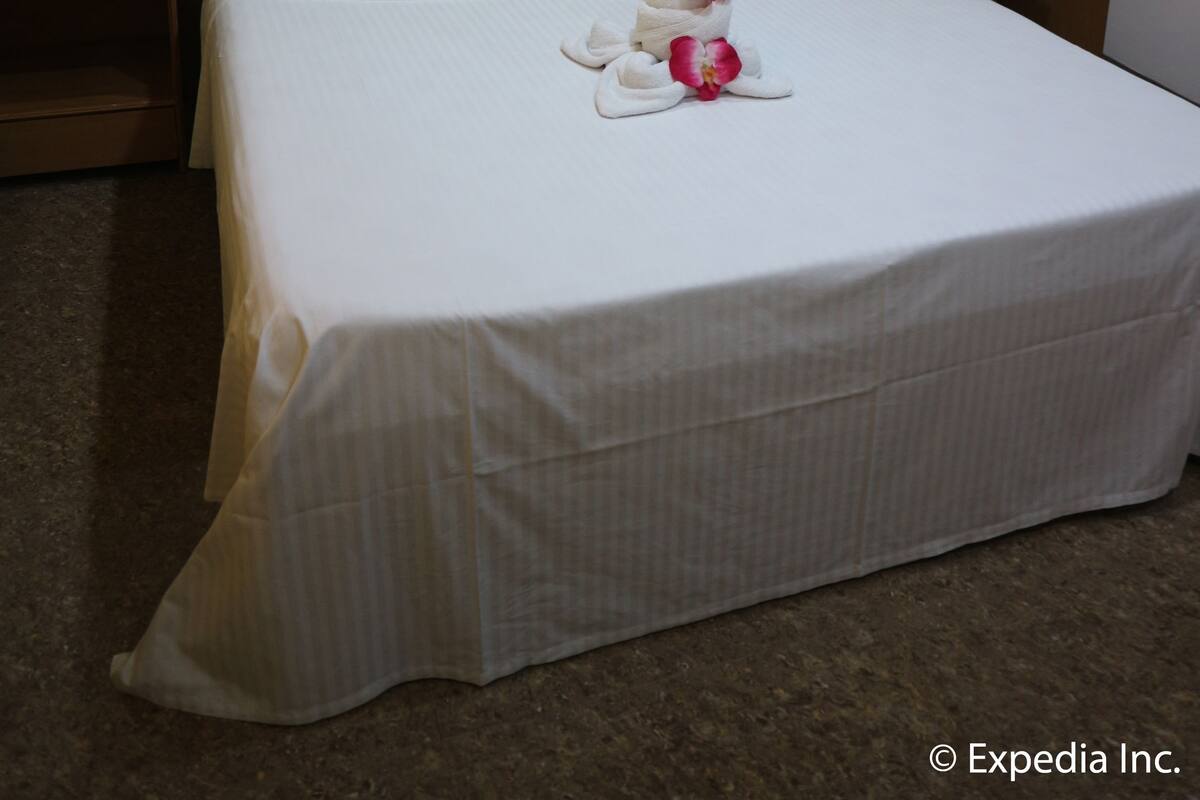 A neatly made bed with white linens and two yellow pillows, an air conditioning unit above, and a small shelf with a mirror.