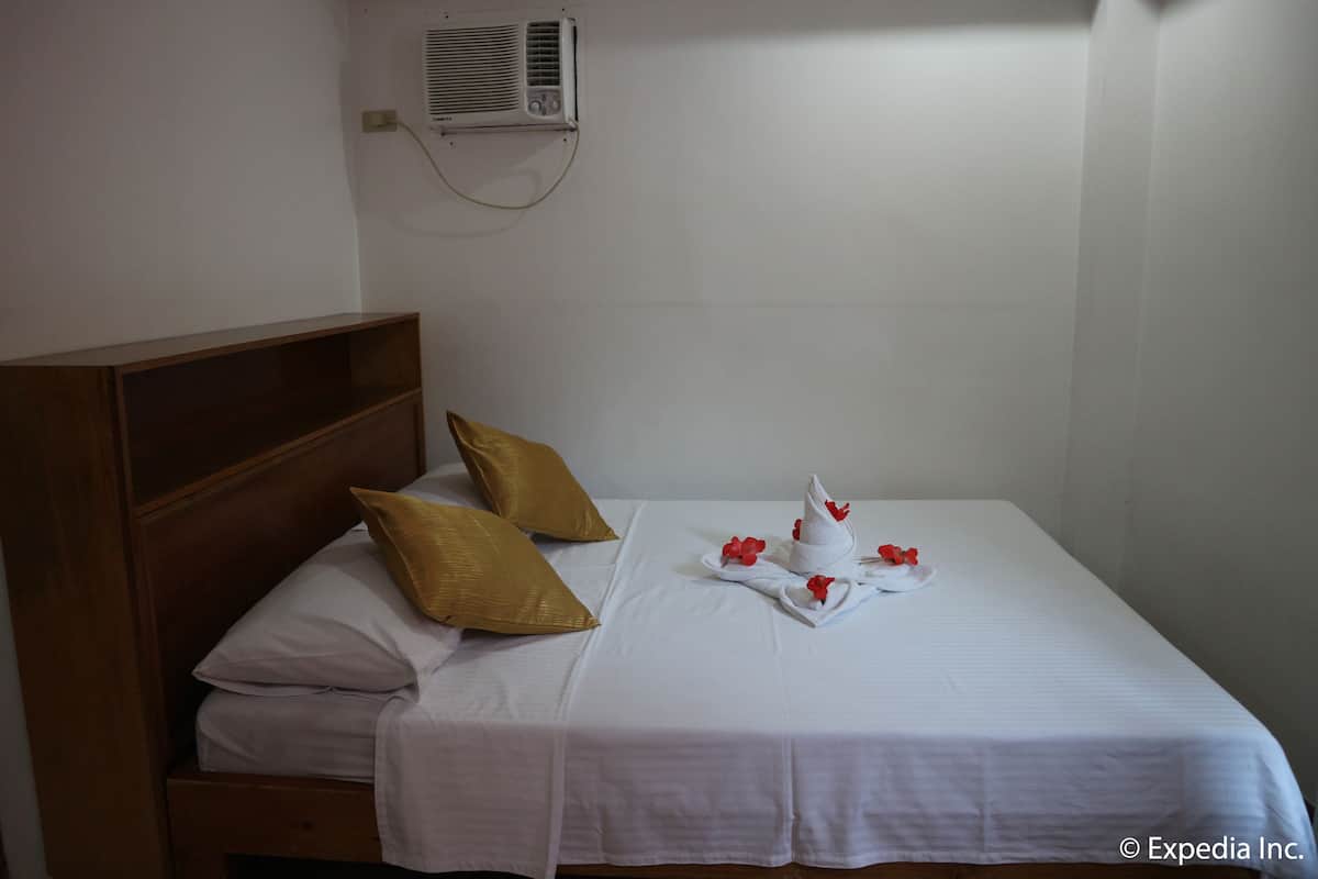 A neatly made bed with white linens, two gold pillows, and a towel with red flowers.