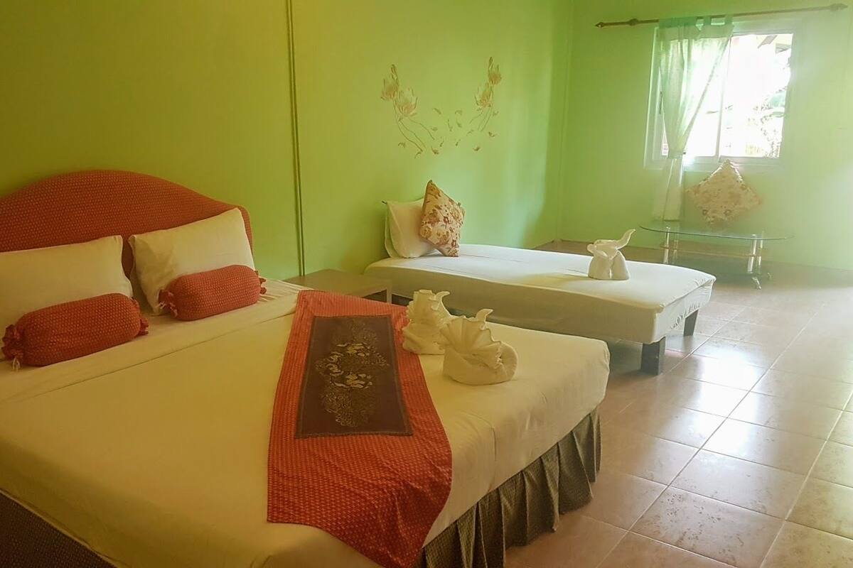 Una habitación de hotel con una cama grande, una cama más pequeña y una zona de estar con una mesa de vidrio.