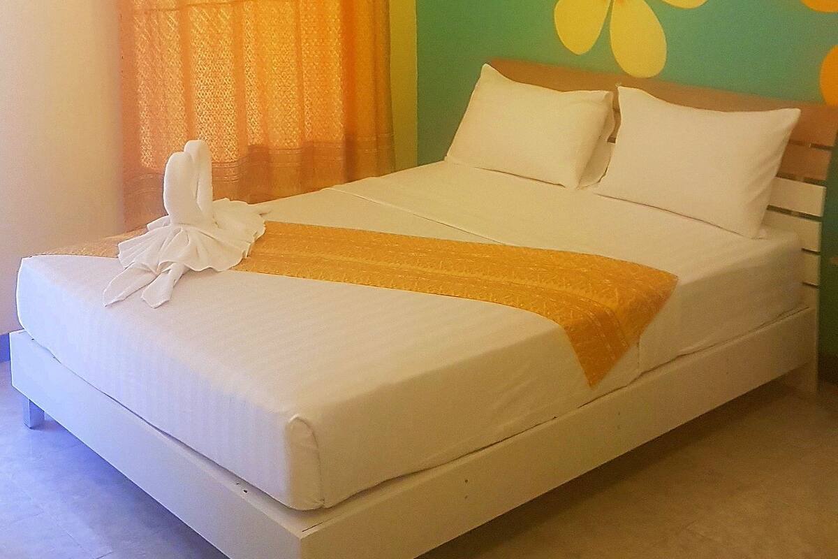 Una cama con ropa de cama blanca, un plaid amarillo y una pared verde decorada con motivos florales.