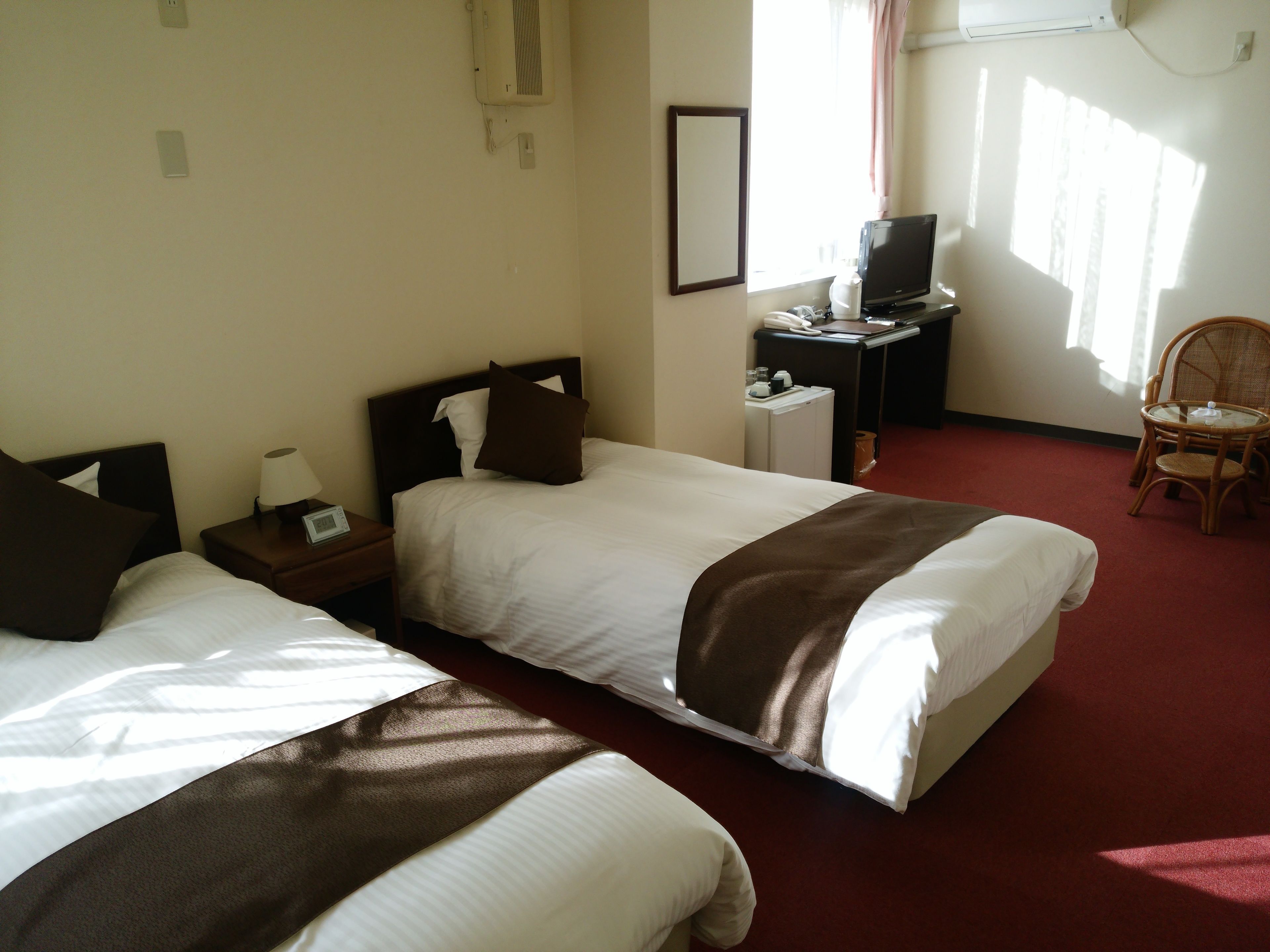 Ein Hotelzimmer mit zwei Betten, einem Schreibtisch mit Computer, einem Stuhl und einem Vorhangfenster.