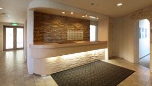 A reception area with a stone wall, a reception desk, and a patterned rug. - Resort Inn North Country (Furano)