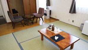 A traditional Japanese-style room with tatami flooring, a low wooden table, a glass-top table, and a chair with a woven backrest. - Resort Inn North Country (Furano)