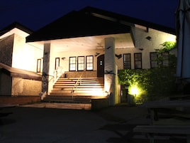 A building with a staircase leading to a covered entrance, a brick wall, and a small garden area with a bench.
