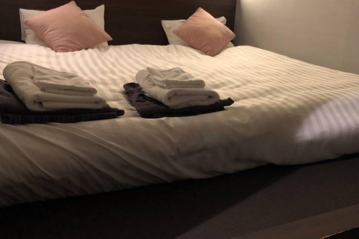 A neatly made bed with pillows, folded towels, and a dark headboard.