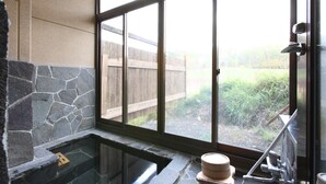 A stone wall, a glass bathtub, and a wooden fence visible through large windows. - Resort Inn North Country (Furano)