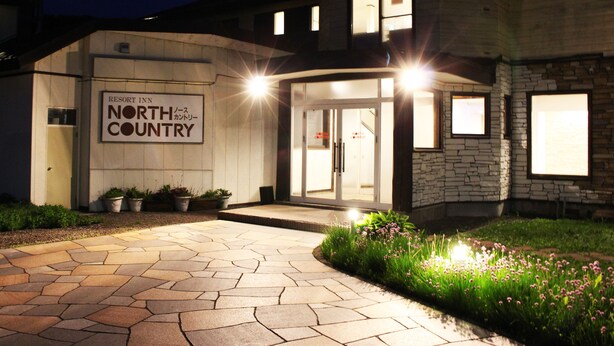A building with a sign reading "Resort Inn North Country" and a stone facade. - Resort Inn North Country (Furano)