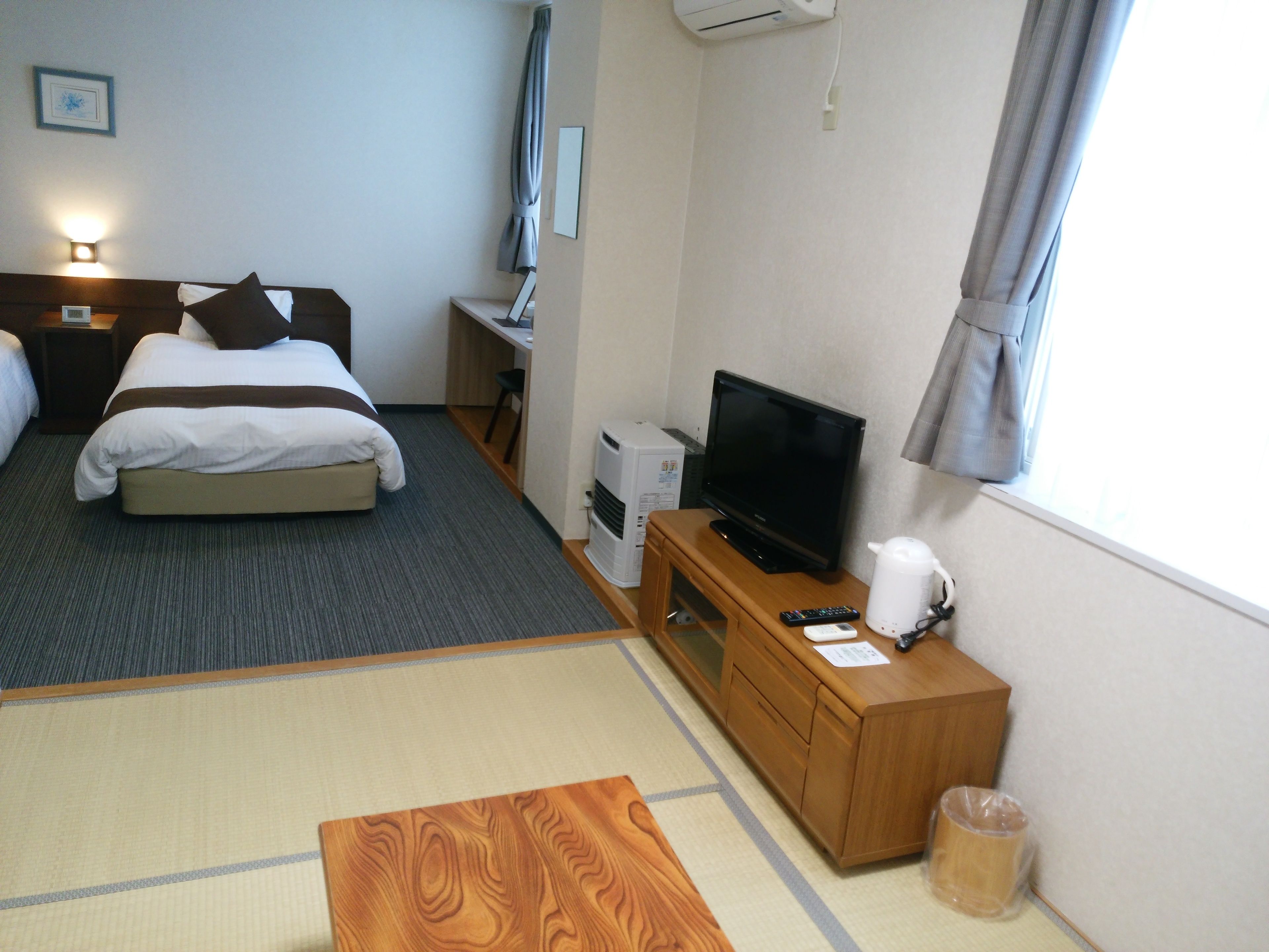Een hotelkamer met een bed, een bureau met een televisie, een kleine verwarming en een raam met gordijnen.