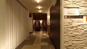 A hallway with a checkered floor, a stone wall, and a sign indicating a restaurant named '80days'. - Resort Inn North Country (Furano)