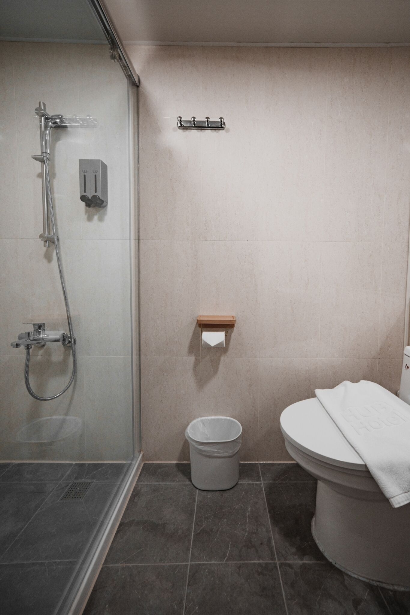 A modern bathroom with a glass-enclosed shower, a toilet, and a small trash bin.