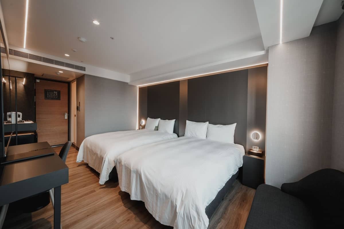 A modern hotel room with two beds, a desk, and a seating area.