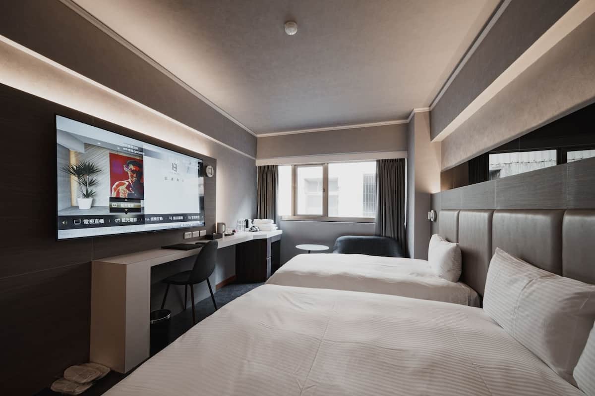 A hotel room with two beds, a desk with a computer, a chair, and a TV mounted on the wall.