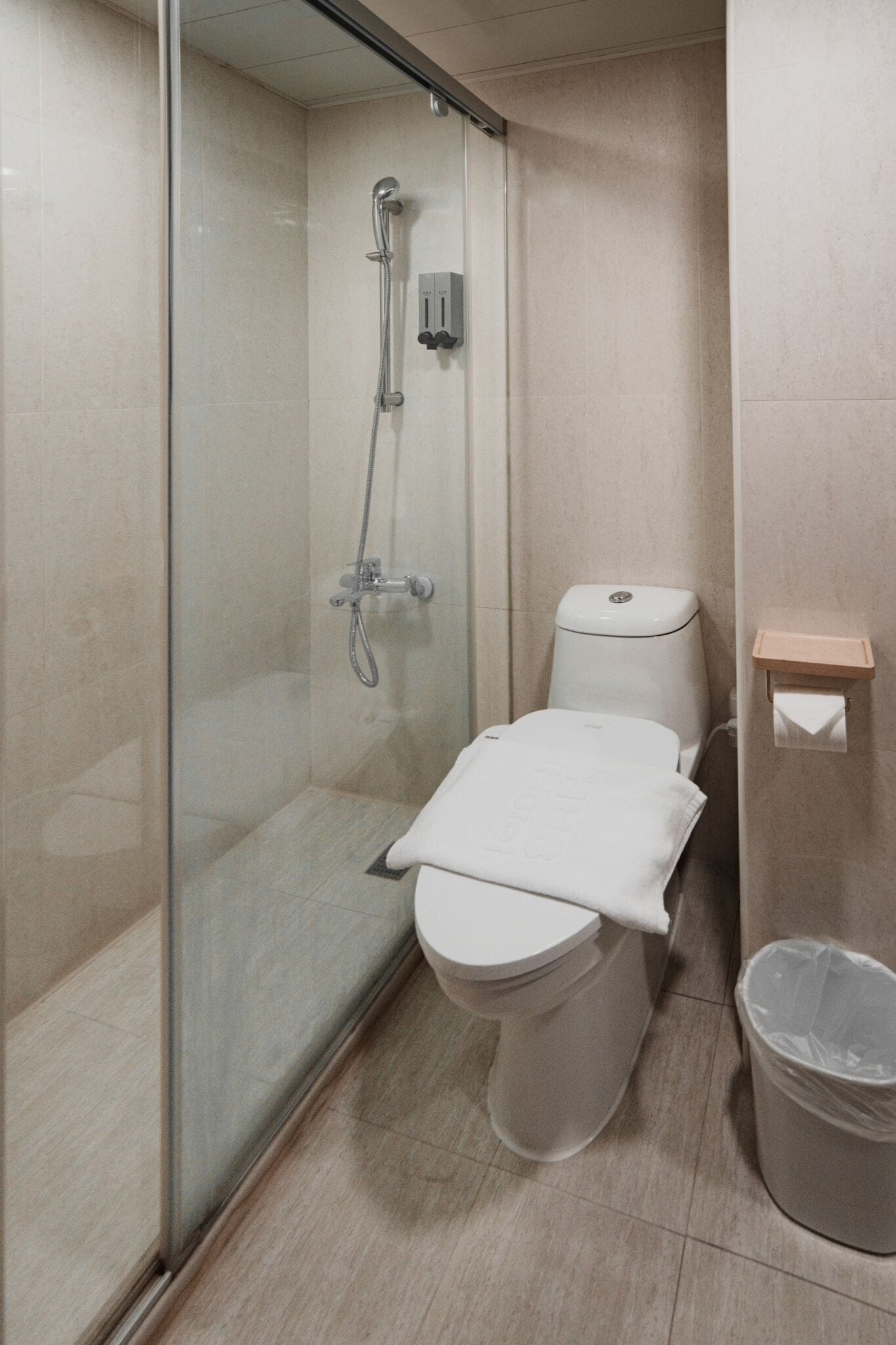 A compact bathroom with a glass-enclosed shower, a toilet, and a trash bin.