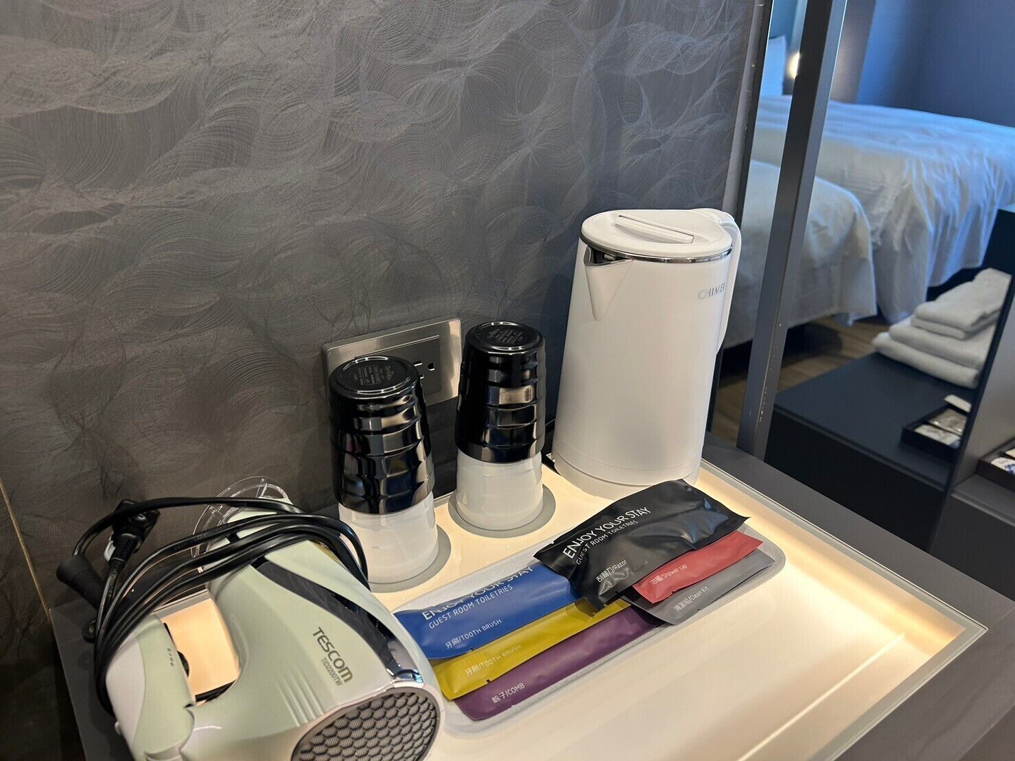 A hotel room with a bed, a minibar, a hairdryer, and toiletries.