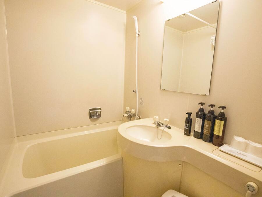 A bathroom with a bathtub, sink, and mirror. There are toiletries on the sink counter.