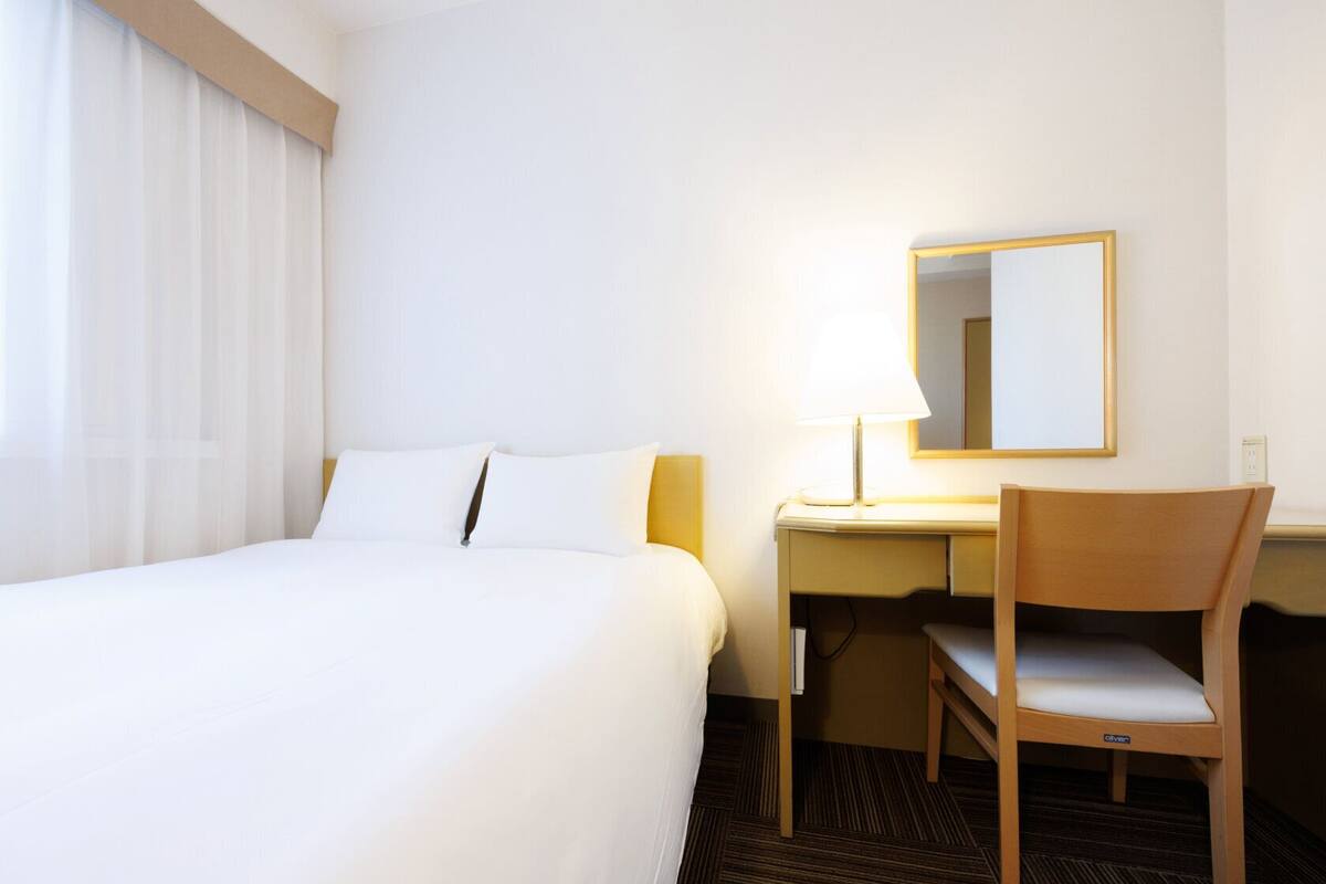 Una habitación de hotel con cama, escritorio, silla y espejo.