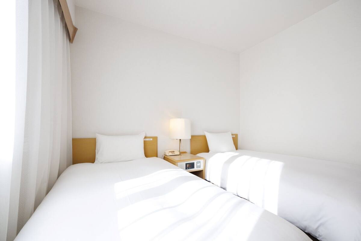 Habitación de hotel con dos camas, una mesita de noche con lámpara, un reloj y un teléfono.