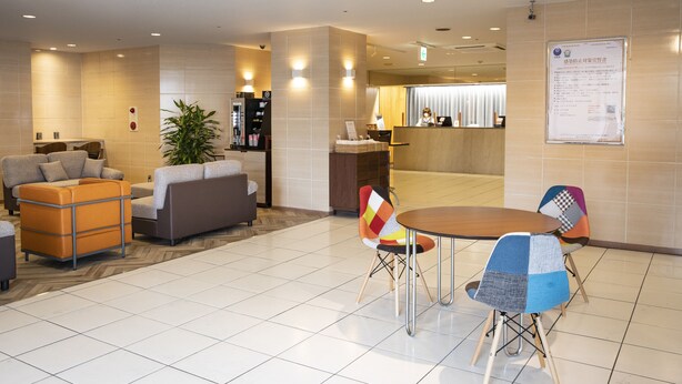 A modern hotel lobby with a reception desk, seating area, and a large potted plant. - Court Hotel Mito (Mito)