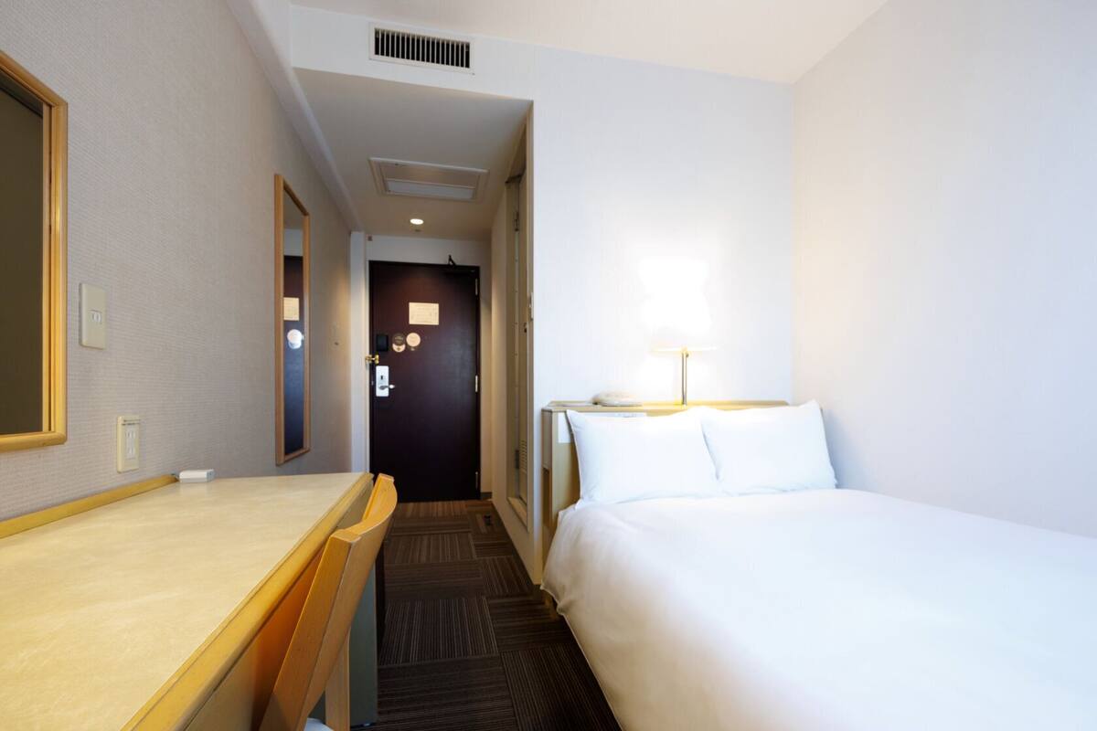 Una habitación de hotel con cama, escritorio, silla, lámpara y puerta.
