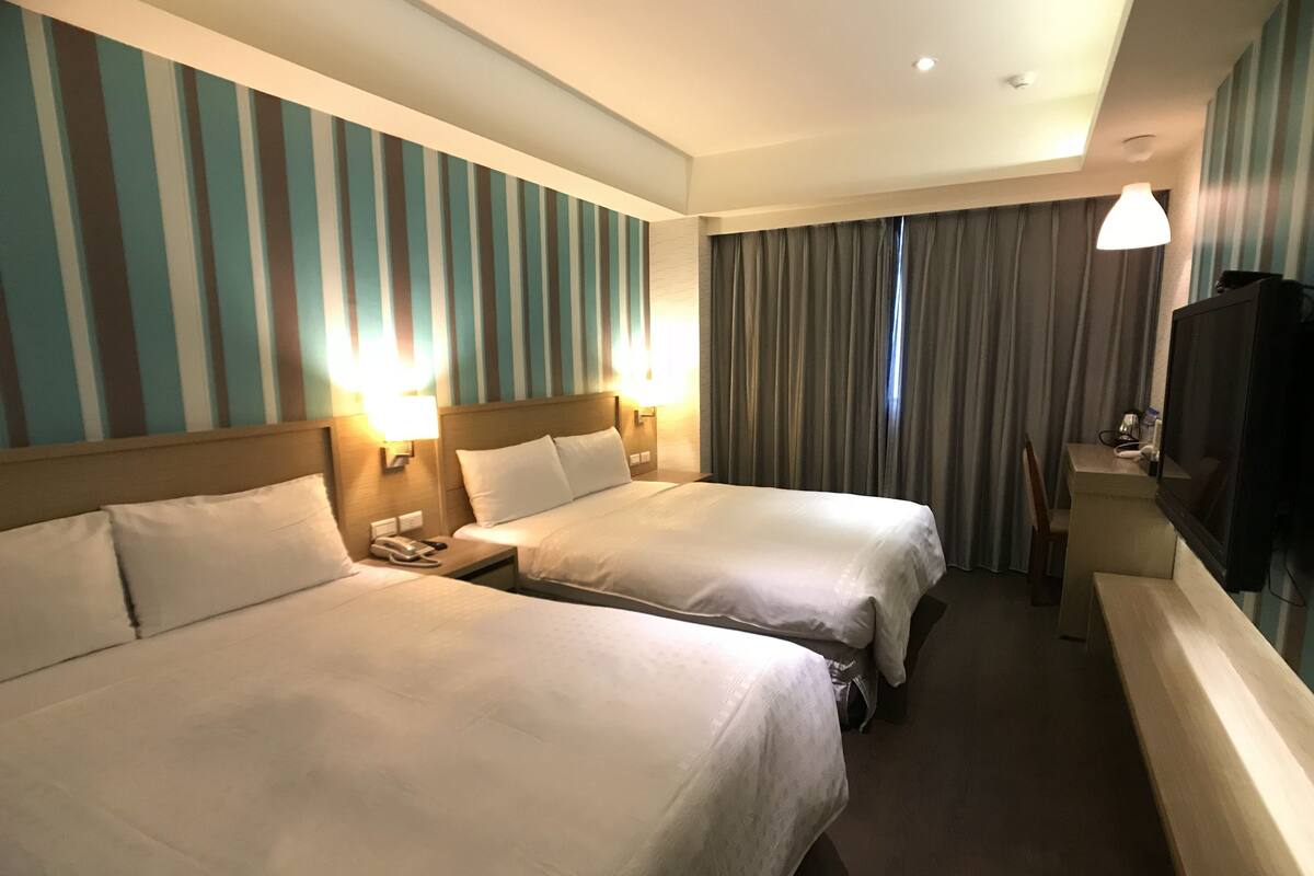 A hotel room with two beds, a desk, a chair, a television, and a mirror.