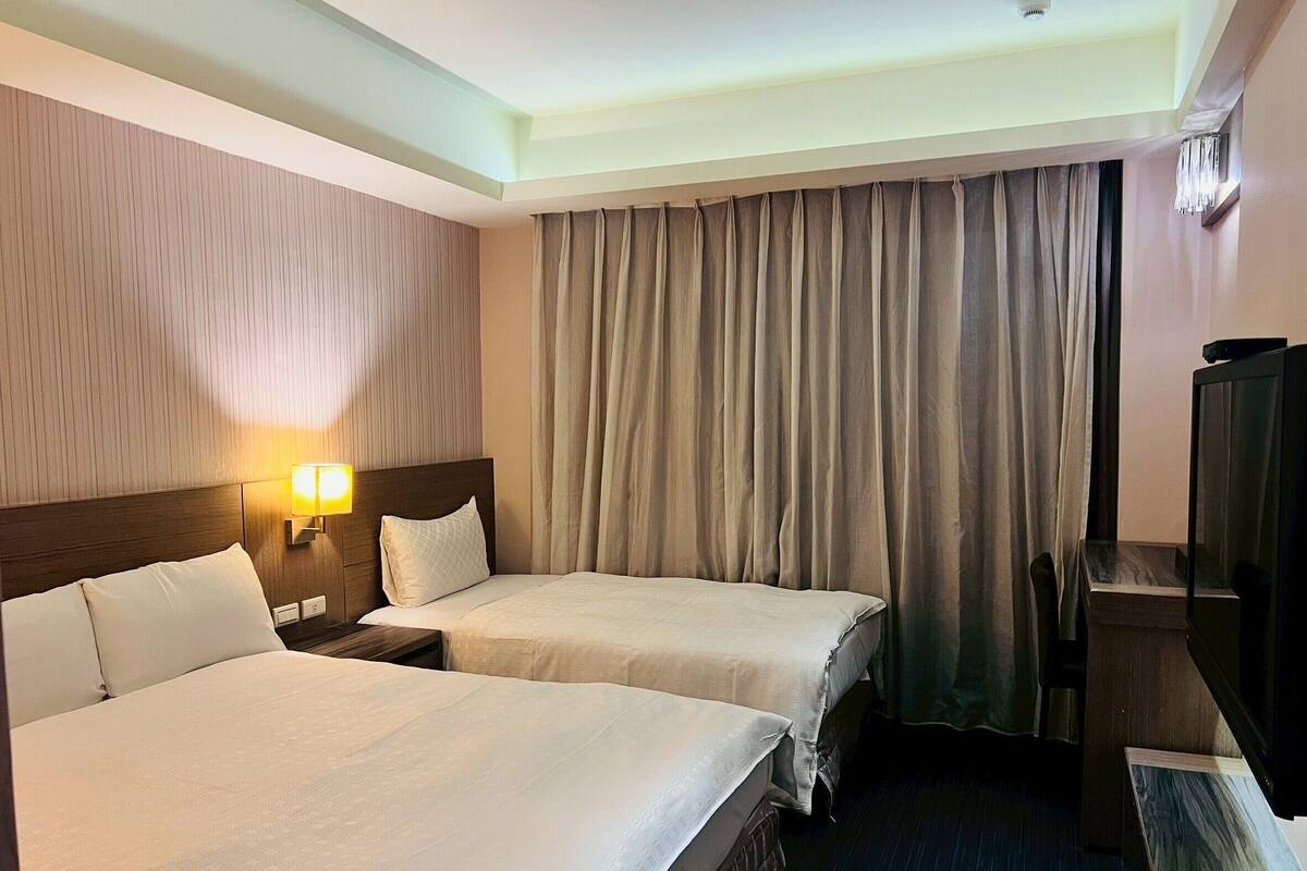 A hotel room with two beds, a TV, and a lamp.