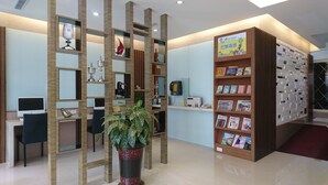 A reception area with a desk, chairs, a potted plant, a telephone, and a bookshelf with magazines. - Paris Business Hotel (Kaohsiung)