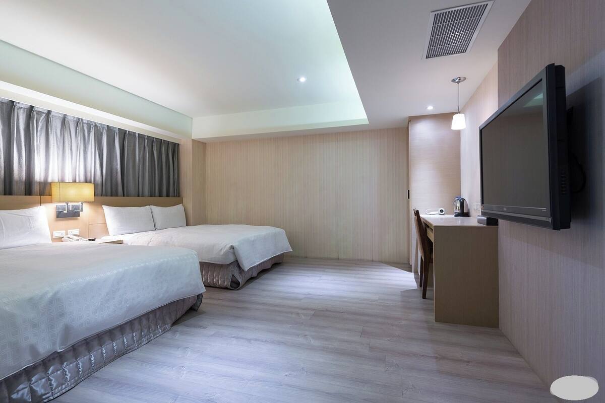 A hotel room with two beds, a TV, a desk with a chair, and a window with curtains.