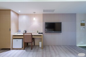 Ein Hotelzimmer mit einem Holztisch, einem Sessel, einem kleinen Kühlschrank, einem an der Wand montierten Fernseher und einem hellen Boden.