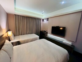 Habitación de hotel con dos camas, televisión, escritorio con lámpara y ventana con cortinas.