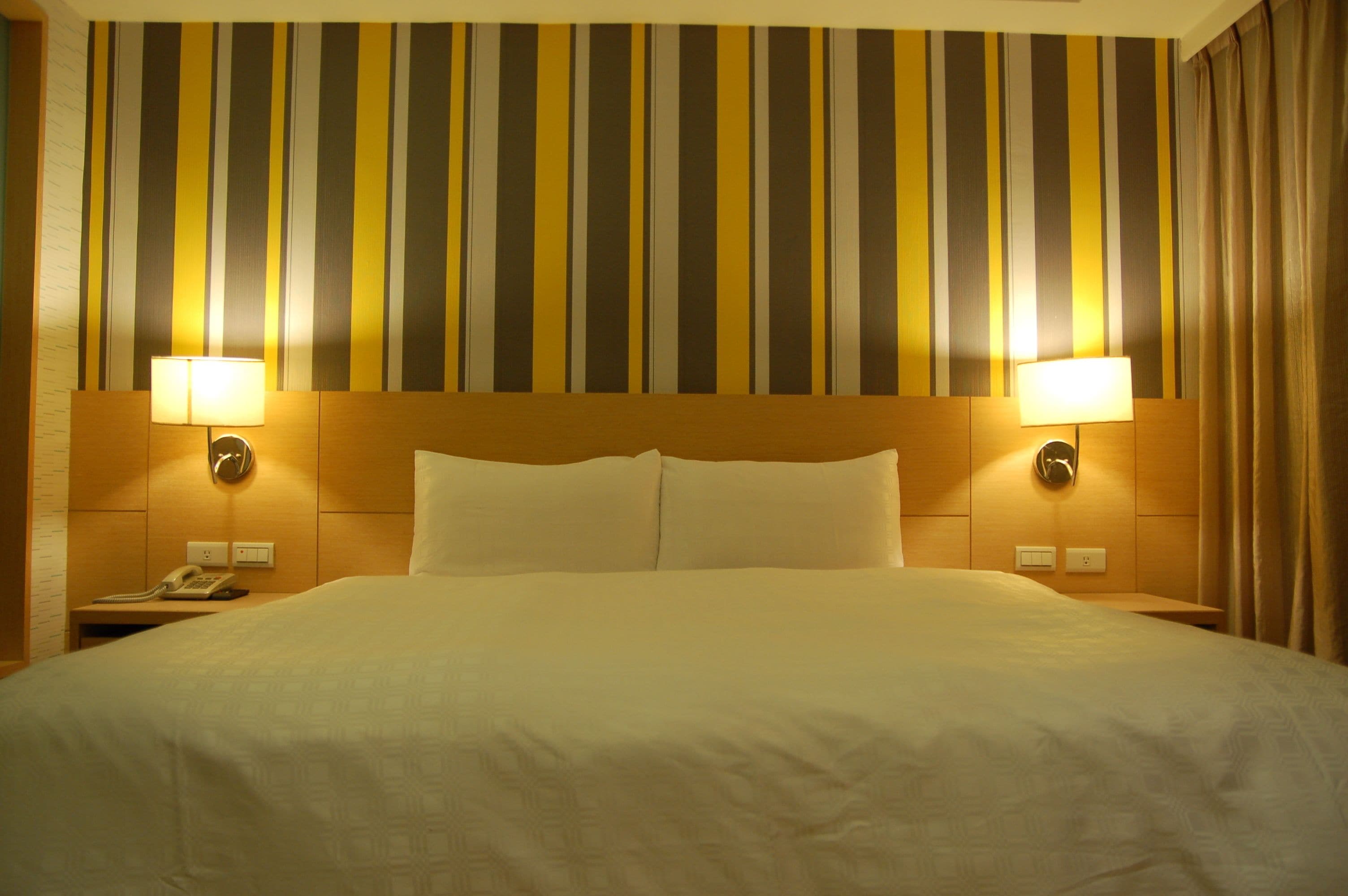 A hotel room with a large bed, two bedside lamps, a telephone, and a striped wall.