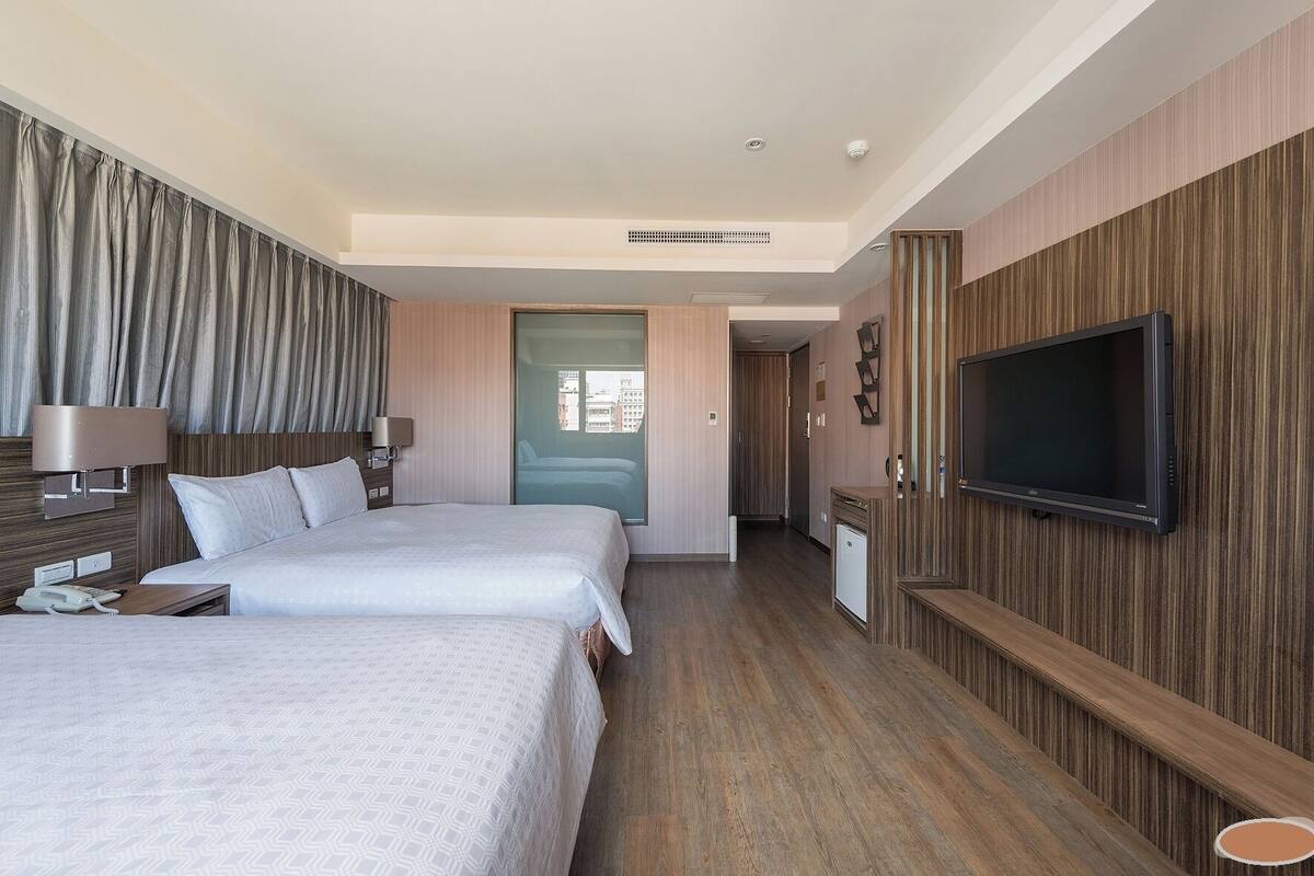 A hotel room with two beds, a TV, a desk, and a bathroom.