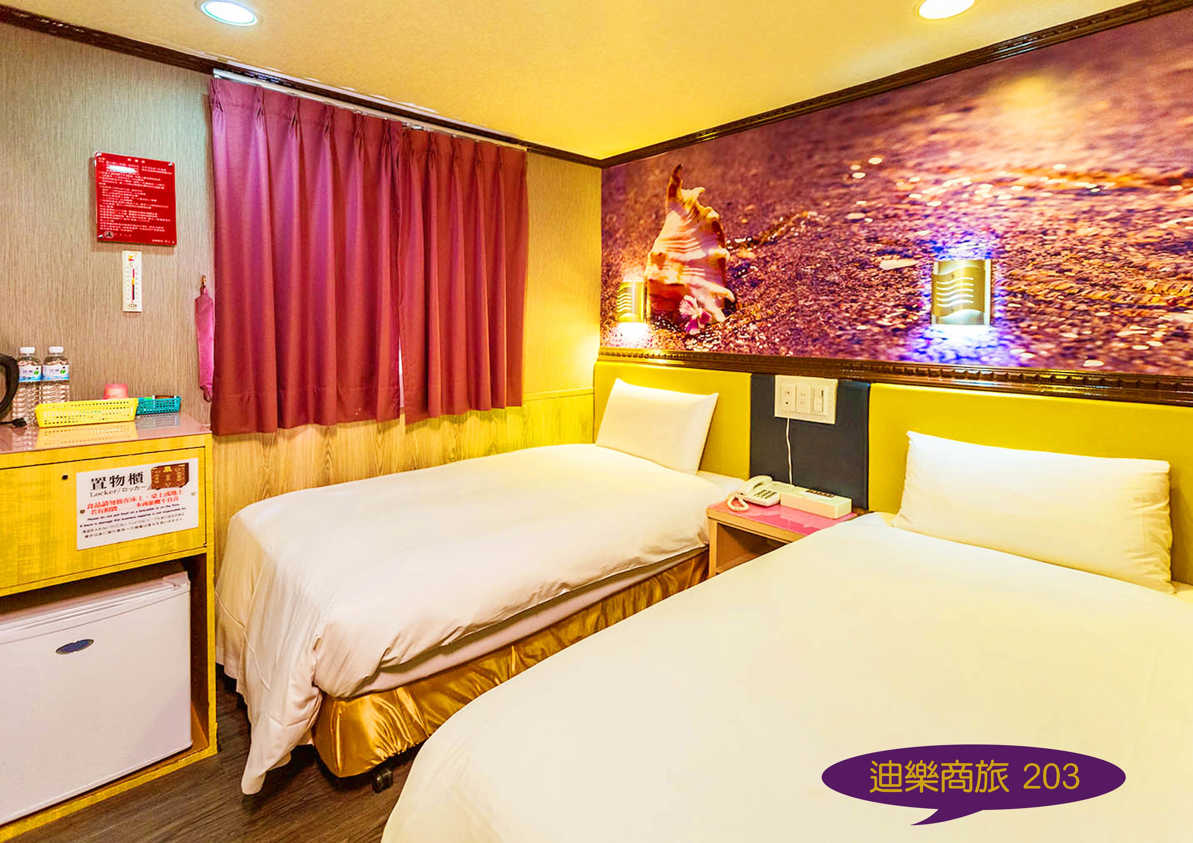 A hotel room with two beds, a wooden desk, a minibar, and a wall with a decorative mural.